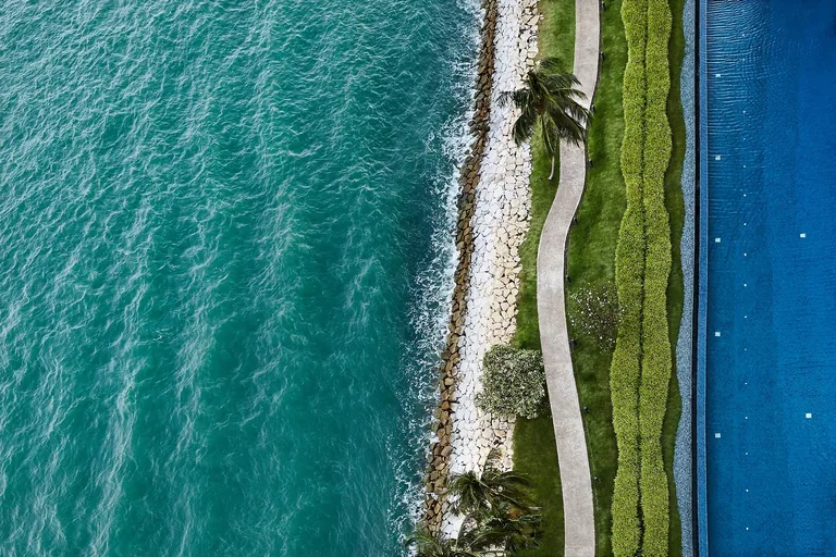Cape Royale, photograph: a top-down view of the sea, the rock breakwater, the seafront path and lawns and the long blue infinity pool