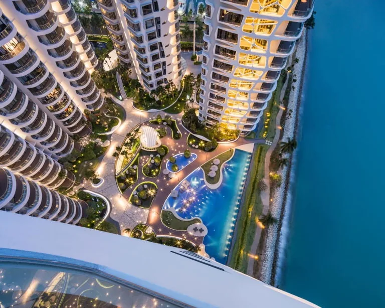 Cape Royale, photograph: the pools, decks and gardens lit at night between the towers, seen from high above, with the sea to the right