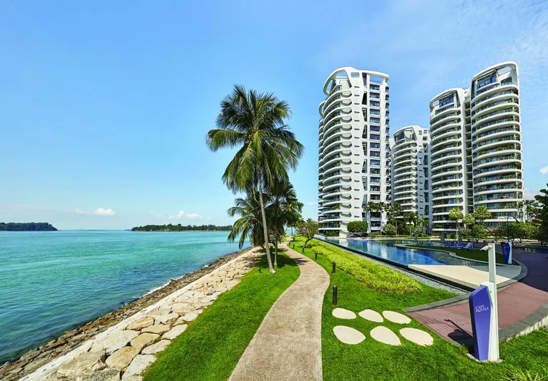Cape Royale, photograph: the curving white towers rising behind the seafront path, the lawns and the edge of the infinity pool, with palms and the sea on the left